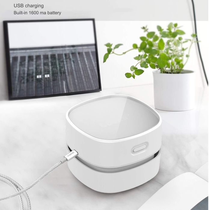 A desktop vacuum placed on a desk with its USB charging cable plugged in.