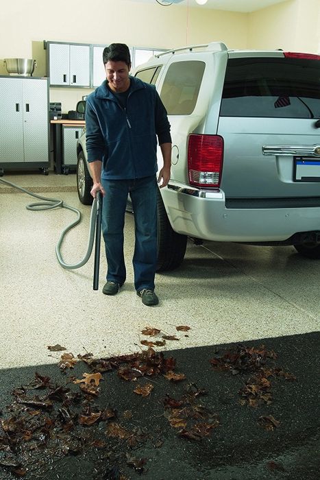 A person using the shop vac to clear leaves from their garage floor