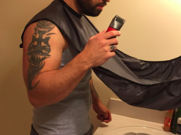 A reviewer’s image showing a person with a beard using the trimmings catcher bib while holding a beard trimmer.