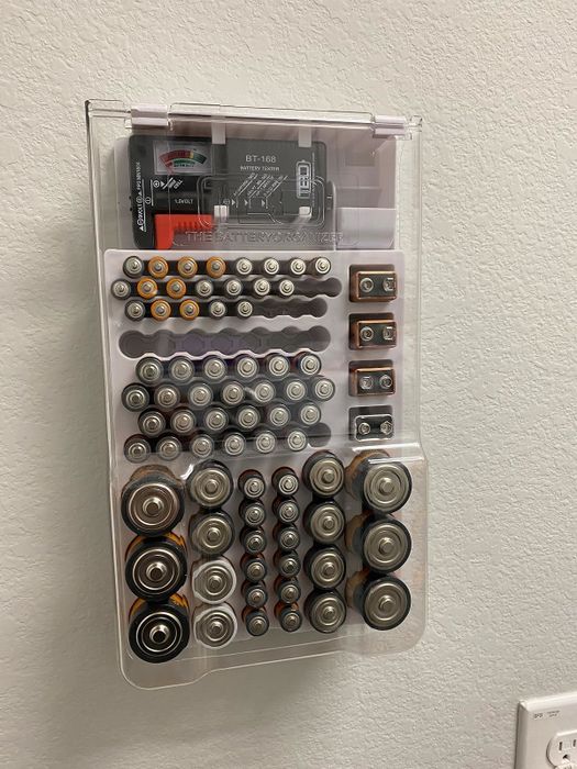A wall-mounted transparent battery organizer filled with different battery sizes
