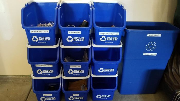 Recycling containers clearly labeled for aluminum cans, electronics, and paper, placed next to a large plastic recycling bin