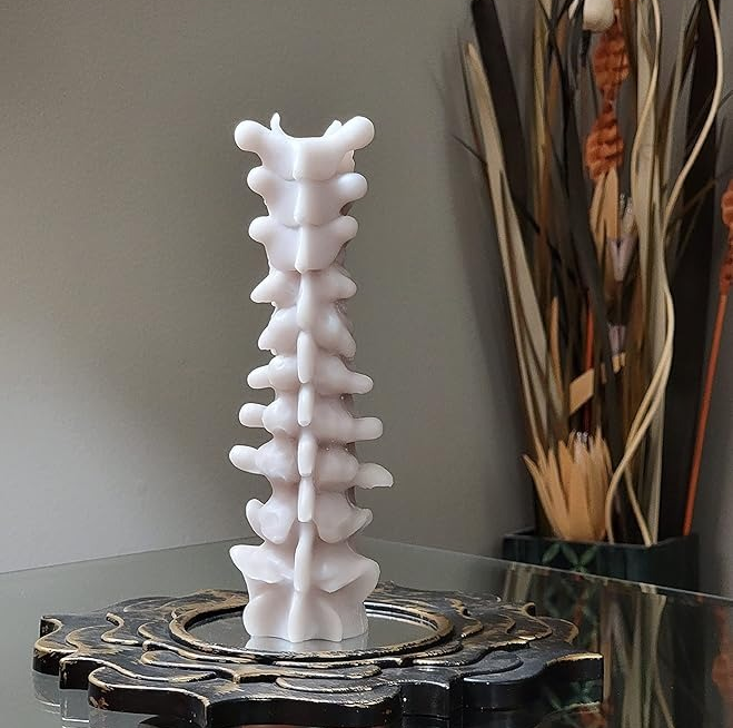 A white sculptural candle in the shape of a spine, displayed on an ornate black base atop a glass table