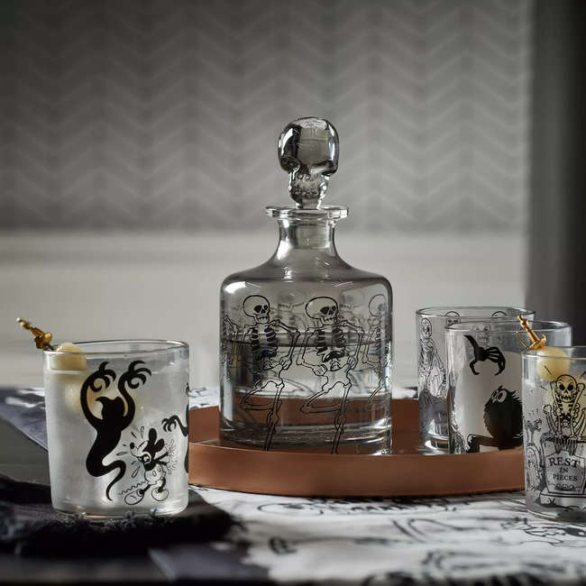 A glass carafe with a sculpted skull stopper and dancing skeletons etched around it