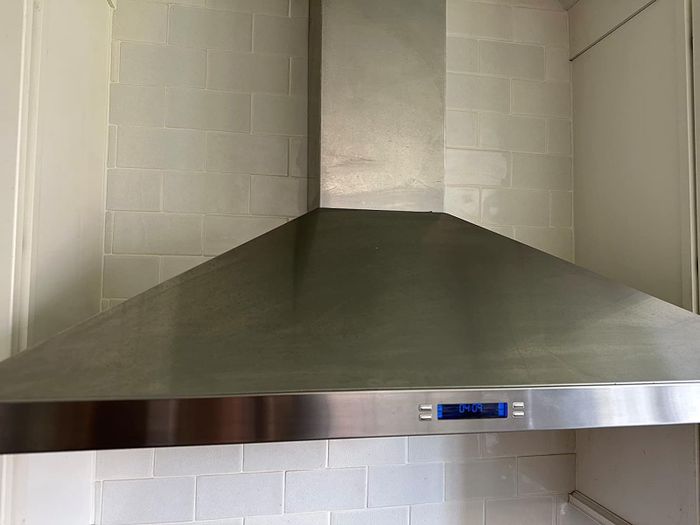 A sleek stainless steel kitchen range hood featuring a digital display panel, mounted above a tiled backsplash