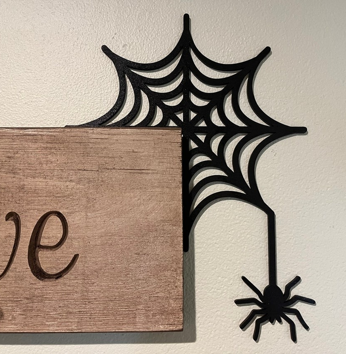 A corner sign adorned with spider web and spider, hugging the edge of another sign