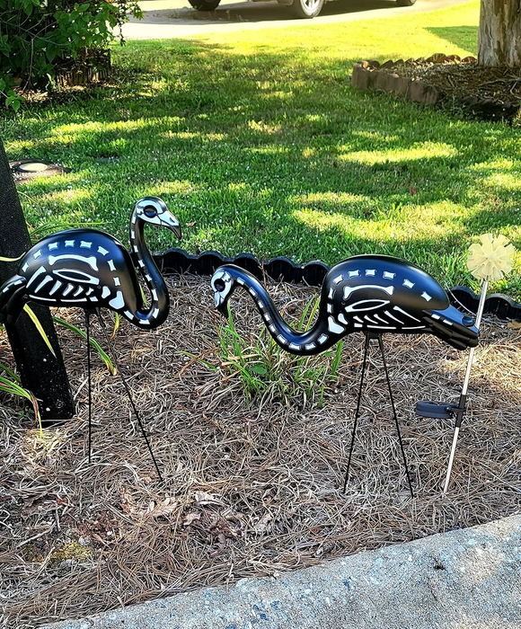 Two metal flamingo yard decorations featuring a skeleton design, placed on a lawn