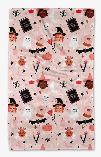 A pink tea towel featuring a delightful design with witches, bats, ghosts, and more