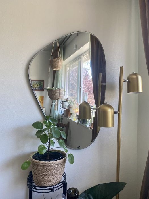 The mirror hanging on a wall, accompanied by a potted plant and lamp in front of it