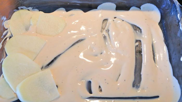 A casserole dish filled with sauce and sliced potatoes.