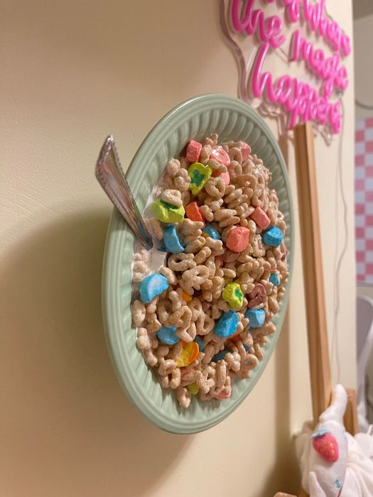 A green plate mounted on the wall holds a serving of cereal with marshmallows and a spoon, set against a backdrop that reads,