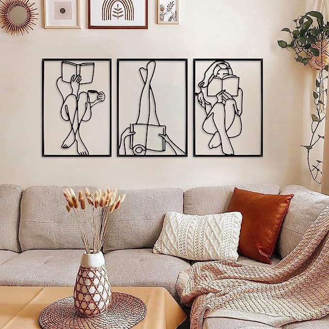 Three metal sculptures depicting a person reading a book in different poses, displayed on a wall above a couch