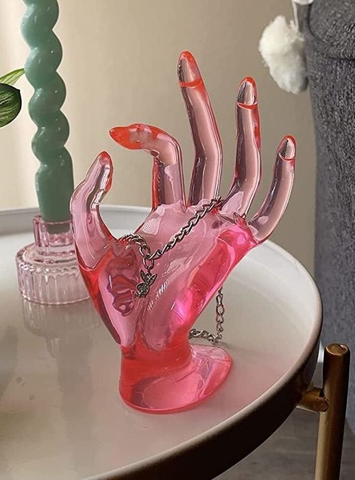 A neon pink plastic hand displayed by a reviewer, adorned with various pieces of jewelry