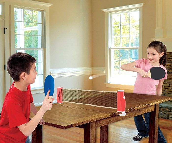 Two kids having a blast playing ping pong, with a net stretched across a wooden table.