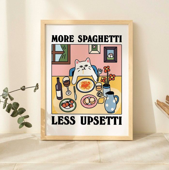 A framed print featuring a cartoon cat eating spaghetti, wine, and side dishes, with the caption