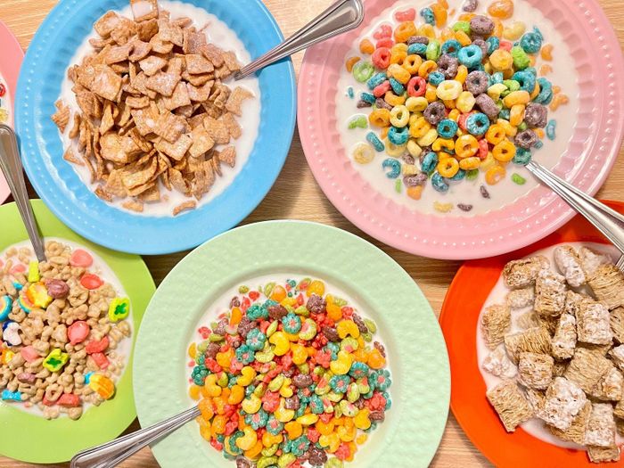 A variety of breakfast cereals with milk in vibrant bowls, including frosted mini-wheats, fruit-flavored loops, and sugary flakes, all beautifully arranged on a table