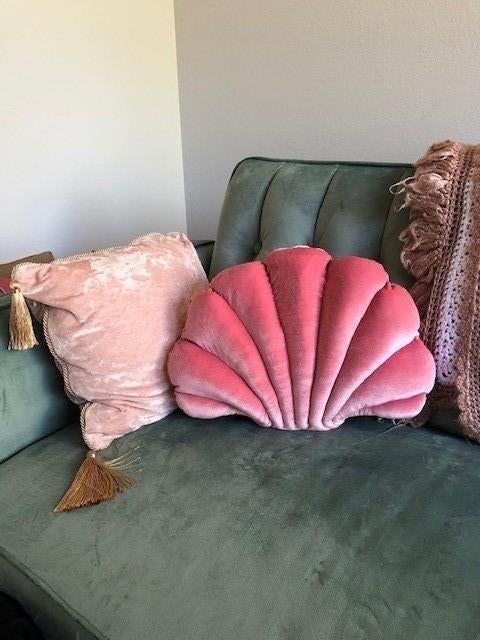 The pink seashell pillow placed on a sofa alongside another cushion