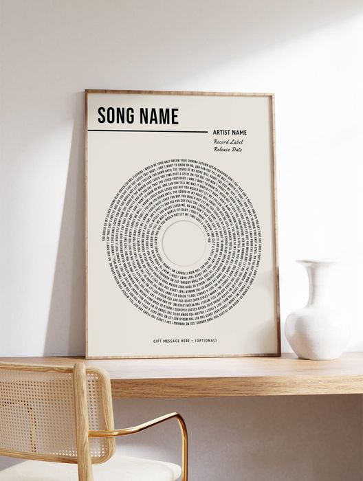 A framed art print featuring song lyrics arranged in a circular design, placed on a wooden shelf with minimalist decor
