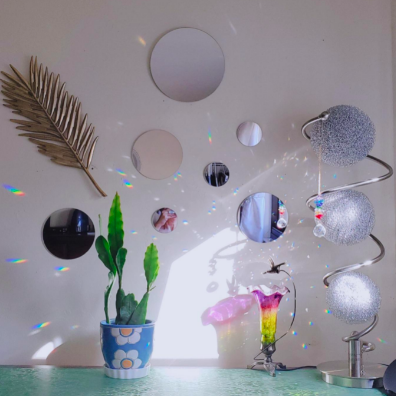 A reviewer's dresser, adorned with round mirrors above the vanity, complemented by a disco ball that reflects light, casting rainbows across the room.