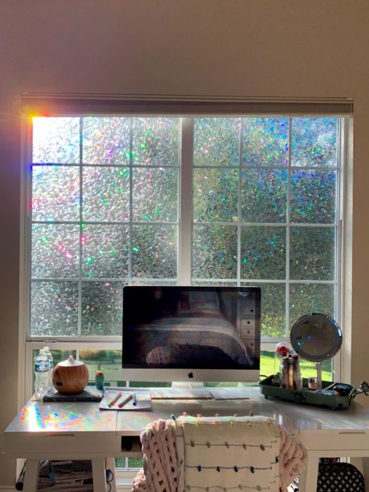 A reviewer's workspace with the window film applied to the overhead window, casting rainbows across the desk