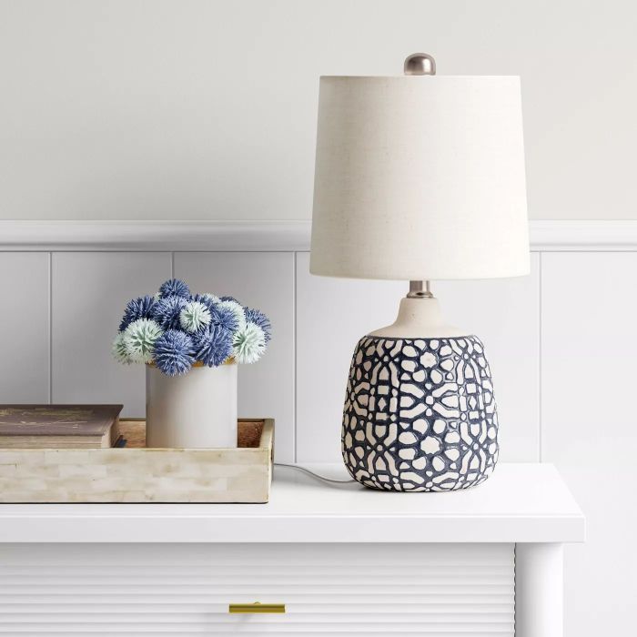 The table lamp with a white shade and a detailed white and blue base placed on a table