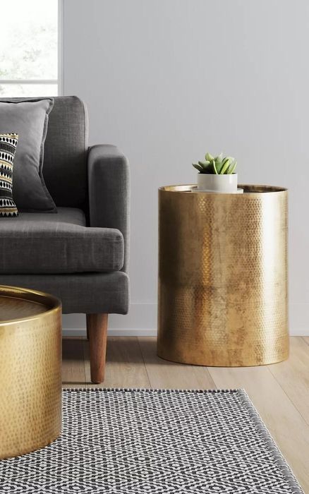A cylindrical gold accent table in a living room, featuring a hammered texture on its exterior.