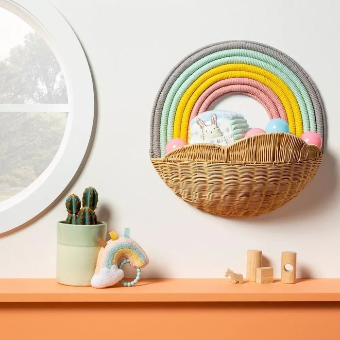A rainbow-colored storage basket hanging on a wall with books and toys stored inside