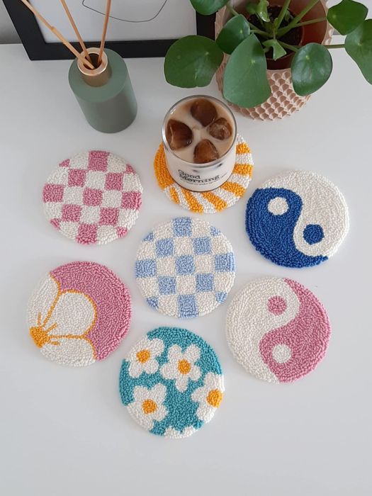 Seven punch needle coasters in an assortment of designs, including floral, yin and yang, and checkered patterns