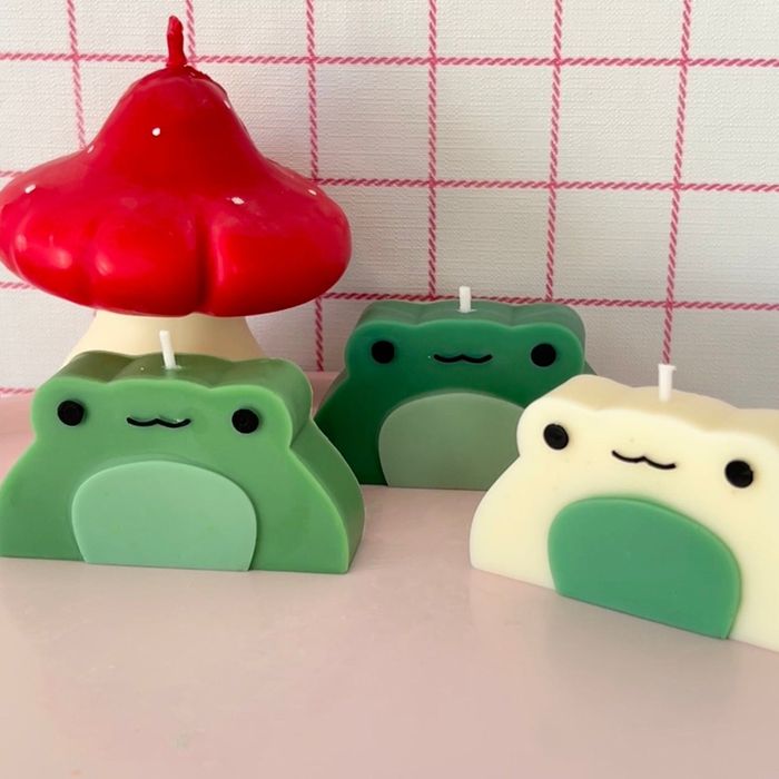Light green, dark green, and white frog candles next to a red mushroom candle