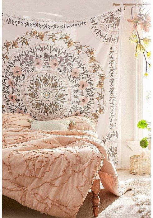 A large white tapestry adorned with pink, green, and brown flowers and leaves, arranged in a circular pattern, hanging on the wall of a bedroom.