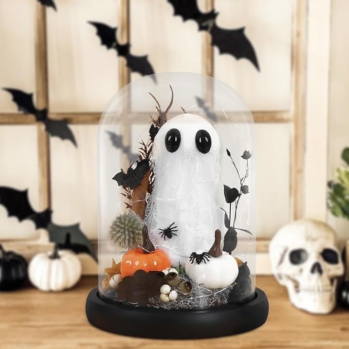A Halloween-themed glass dome featuring a ghost figure, mini pumpkins, a skull, and bats