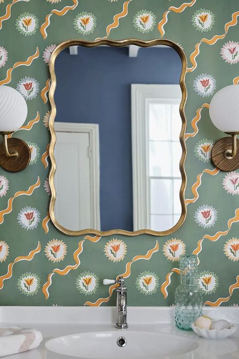 The wall mirror positioned above a sink against patterned wallpaper