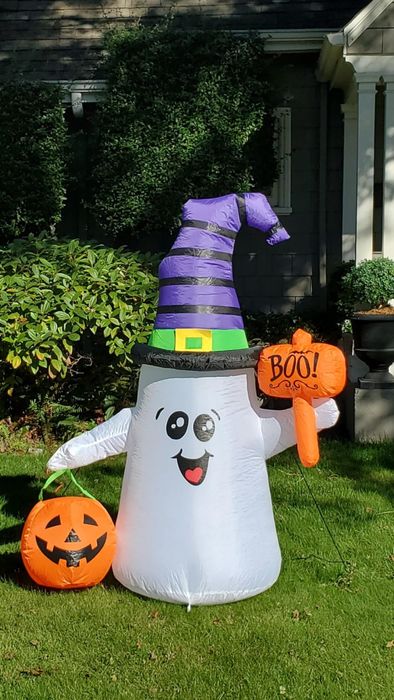 A yard display featuring an inflatable ghost donning a striped witch hat and clutching a 