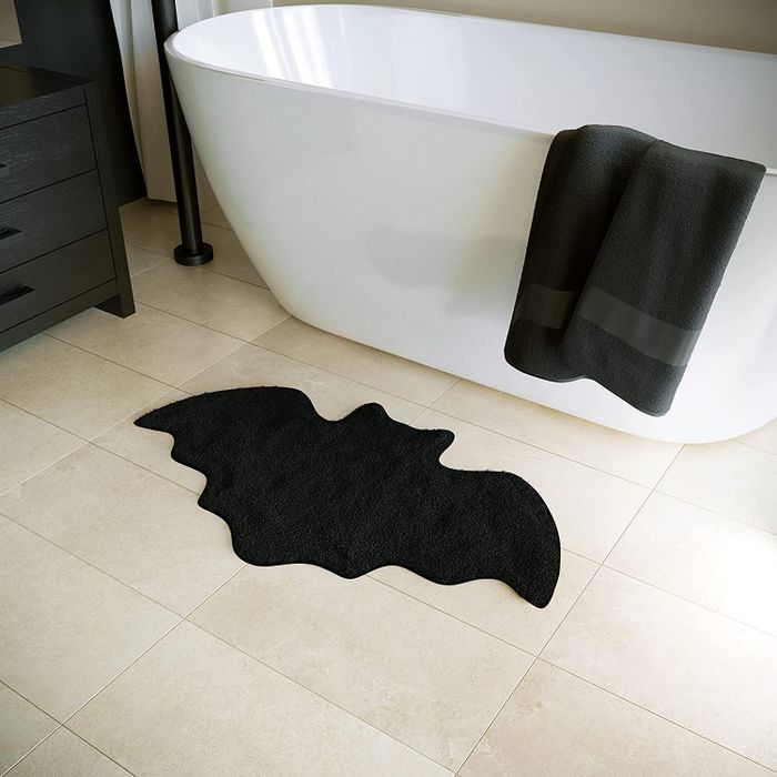 a bat-shaped bath mat placed in front of a bathtub