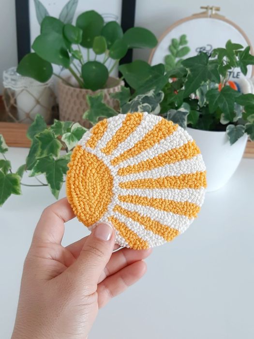 A person holding up the punch needle coaster featuring a yellow sun design