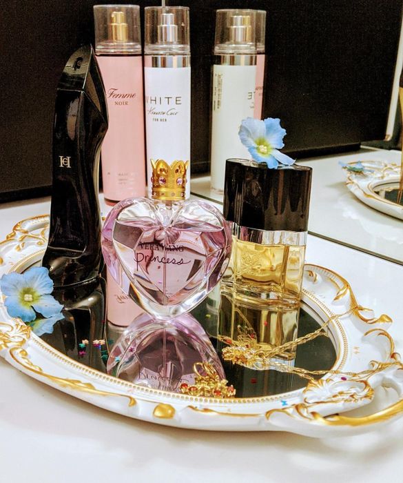 A photo of perfume and other small items arranged on a white and gold mirror, repurposed as a stylish tray.