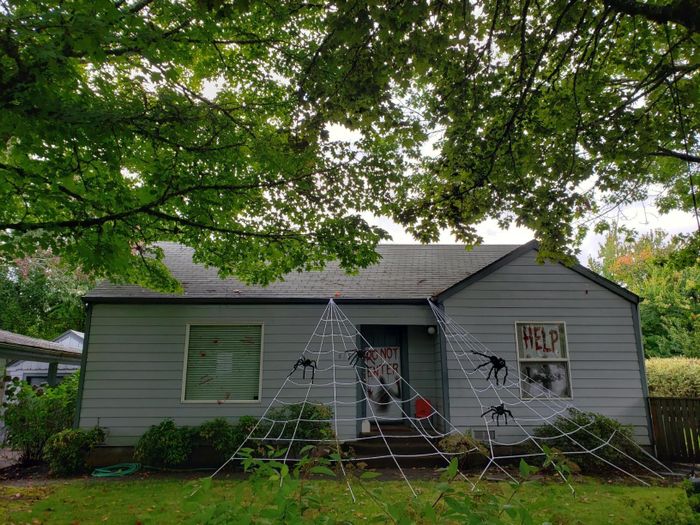 A Halloween-decorated house featuring large spider webs, window spiders, and signs reading 