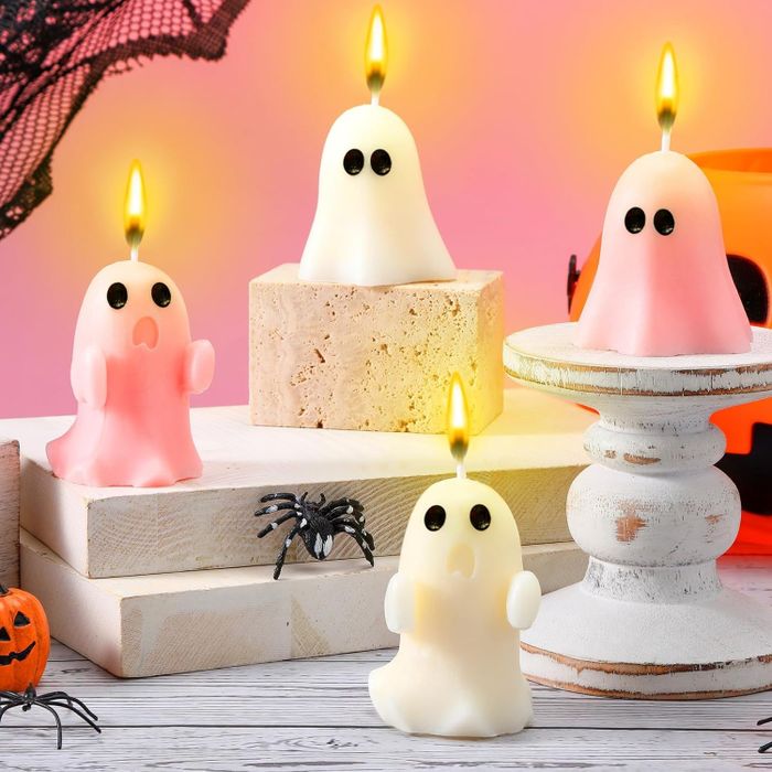 Halloween-themed ghost candles with glowing wicks arranged on wooden blocks and a pedestal, accompanied by a fake spider and pumpkin decorations