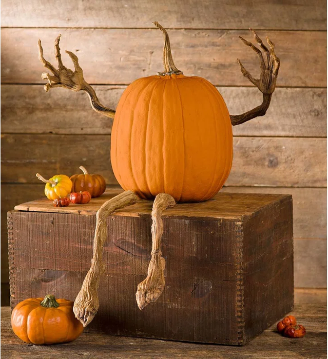 Pumpkin decor featuring realistic hand and foot-like appendages placed on a wooden crate, surrounded by smaller pumpkins