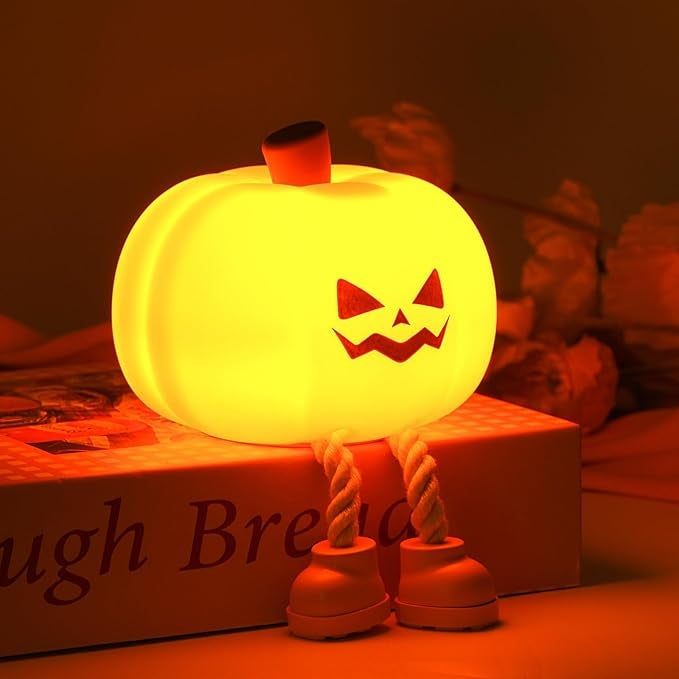 A glowing pumpkin lamp with a jack-o'-lantern face and rope legs, placed on a book for a festive Halloween vibe