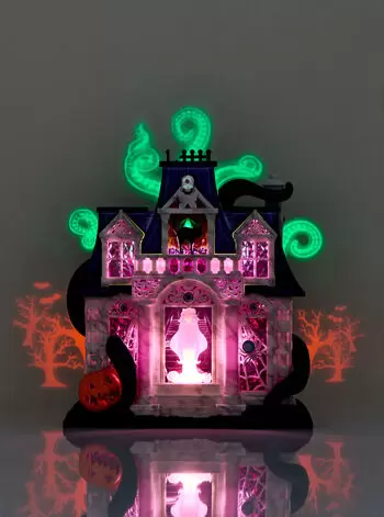 A decorative haunted house figurine glowing with green and purple lights, surrounded by silhouette trees and a pumpkin, perfect for spooky home decor