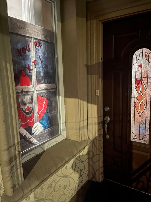 A chilling Halloween decoration of a creepy clown in a window beside a front door, with 
