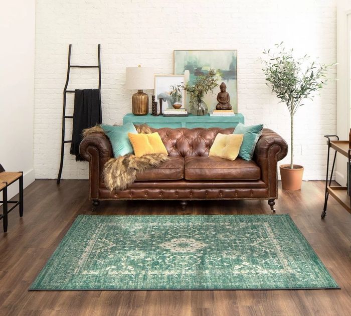 The green area rug with a light floral pattern and distressed details, displayed in a living room