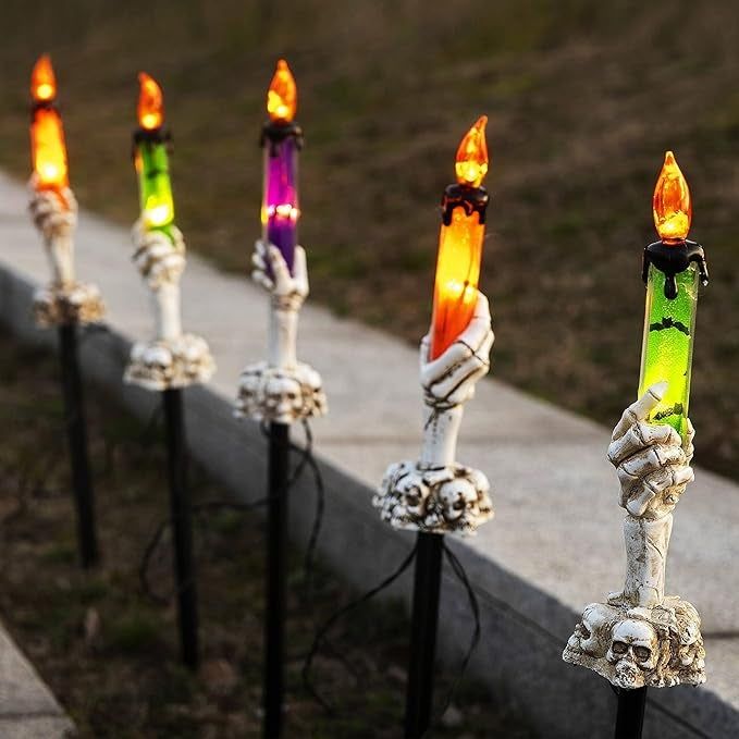Halloween pathway lights shaped like skeleton hands holding candles, with vibrant orange flames