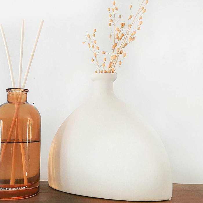 A sleek white hourglass-shaped vase elegantly displaying dried plant sprigs.