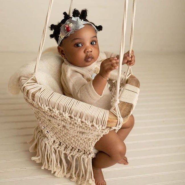 A baby seated in a chair with a wooden frame and macramé details