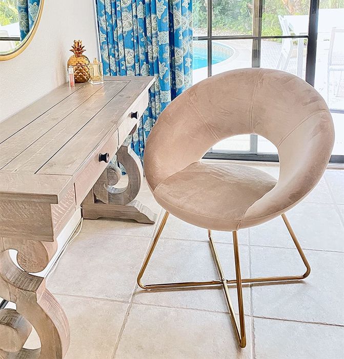 A reviewer’s photo of the beige velvet chair with gold legs, placed in front of a desk.