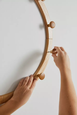 A person’s hands adjusting a round wooden wall mirror.