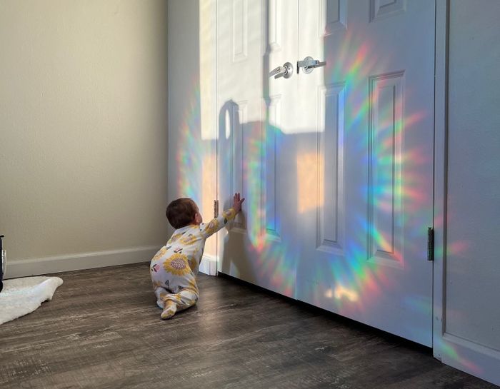 A baby reaches out to touch a rainbow projected on a door