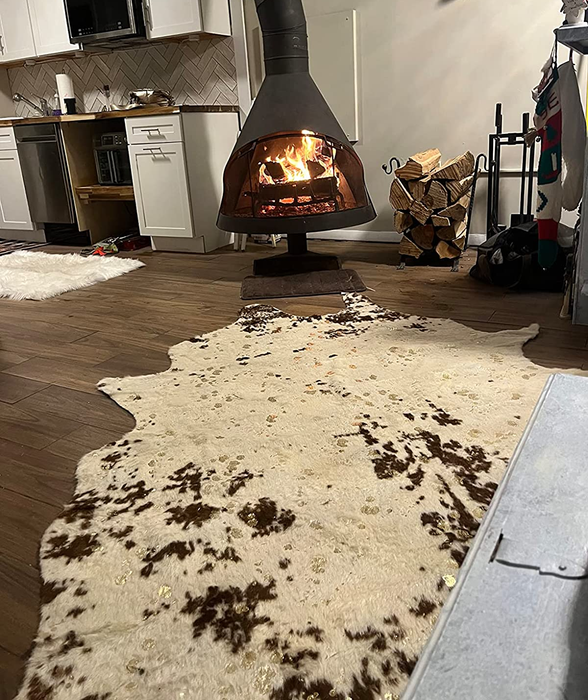 A reviewer’s photo of the brown and white rug placed in front of a fireplace.