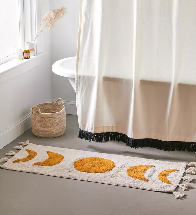 The moon phase bath mat laid out in front of a bathtub.